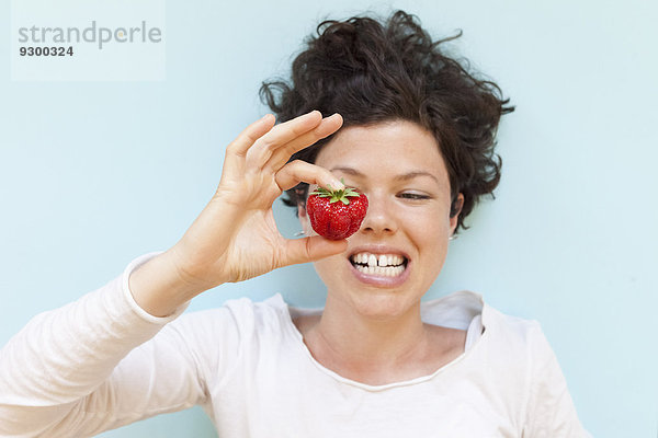 Eine Frau  die die Zähne zusammendrückt  während sie Erdbeere auf blauem Hintergrund hält.