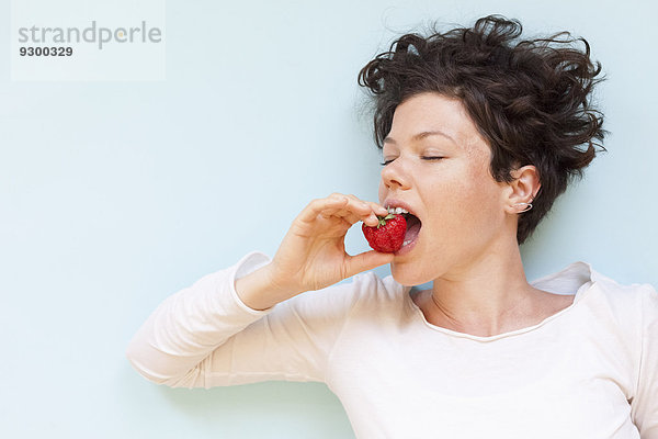 Eine Frau  die Erdbeere auf blauem Hintergrund isst.