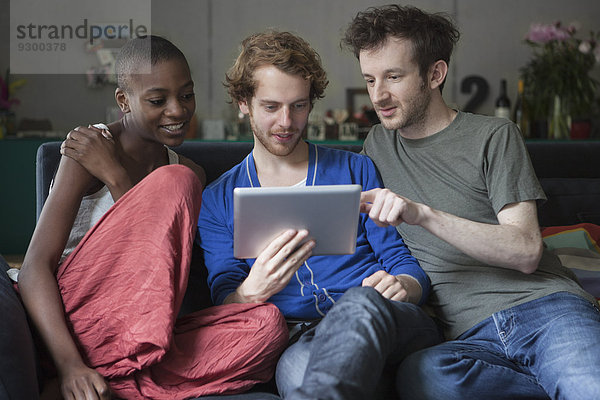 Freunde  die das digitale Tablett gemeinsam auf dem Sofa zu Hause benutzen