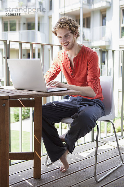 Lächelnder Mann mit Laptop auf der Veranda