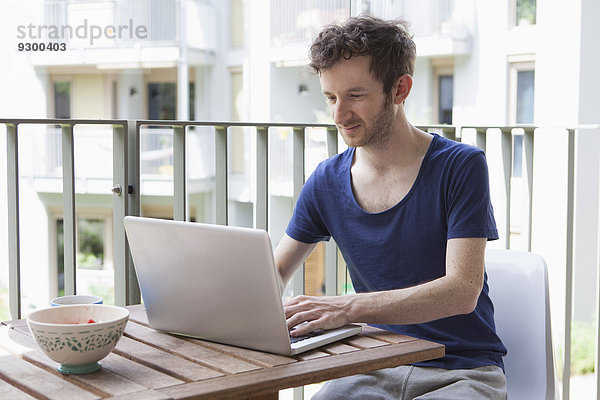 Junger Mann mit Laptop auf der Veranda