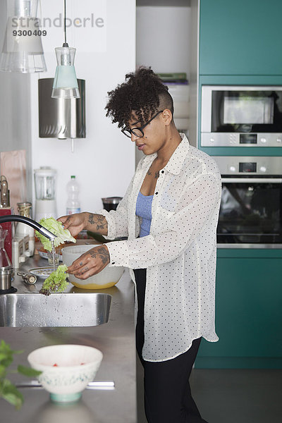 Junge Frau wäscht Gemüse in der Küche