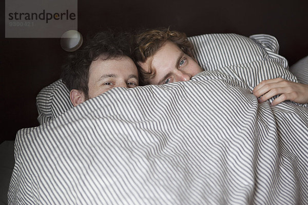Hochwinkliges Porträt eines jungen schwulen Paares  das durch ein Bettlaken blickt