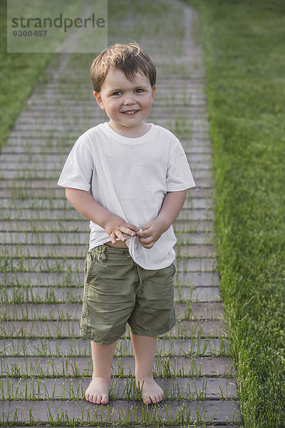 Porträt eines süßen Jungen  der auf einem Fußweg im Park steht.