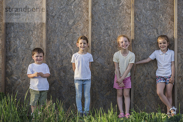 Porträt niedlicher Kinder an der Holzwand stehend