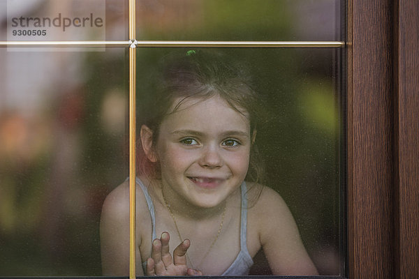 Glückliches kleines Mädchen  das aus dem Fenster schaut.