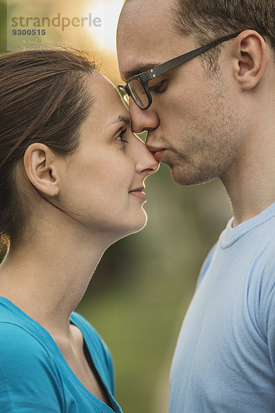 Seitenansicht des jungen Mannes  der die Frau auf der Nase im Park küsst.