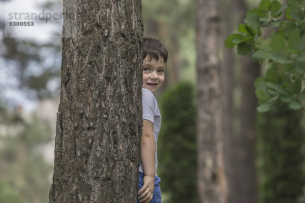 Süßer Junge versteckt sich hinter Baumstamm im Park