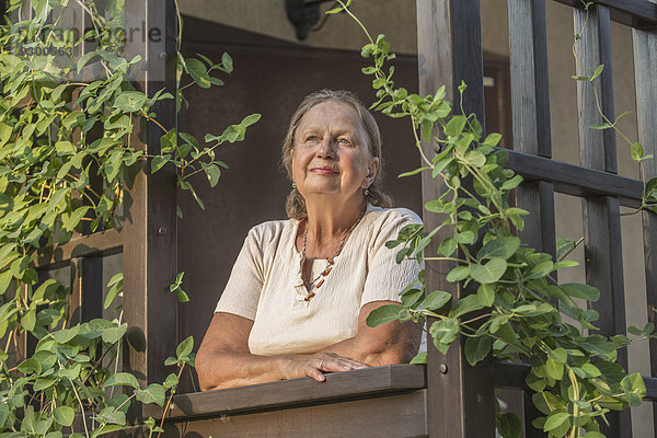 Nachdenkliche Seniorin schaut weg  während sie auf dem Balkon steht.