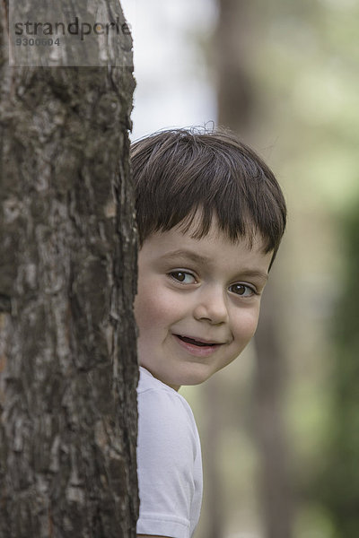 Süßer Junge versteckt sich hinter Baumstamm im Park