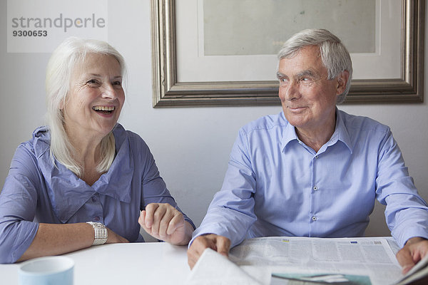 Glückliches Seniorenpaar mit Zeitung am Tisch im Haus