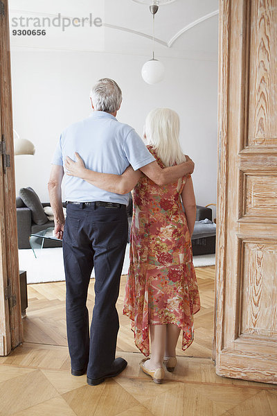 Durchgehende Rückansicht des älteren Paares  das mit den Armen am Eingang des Hauses steht.