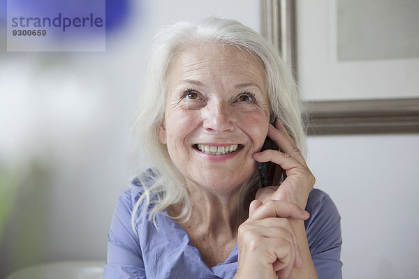 Glückliche Seniorin schaut auf  während sie zu Hause ans Handy geht.