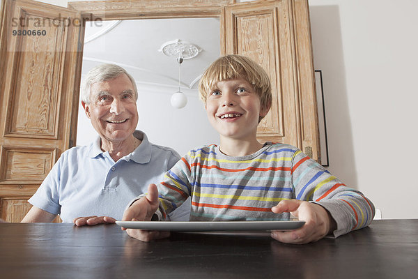 Glücklicher älterer Mann sitzend durch Enkel mit digitalem Tablett zu Hause