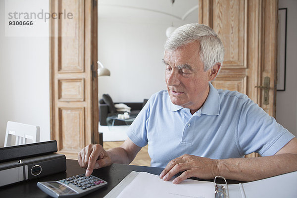 Senior Mann mit Taschenrechner zur Berechnung der Hausfinanzen am Tisch