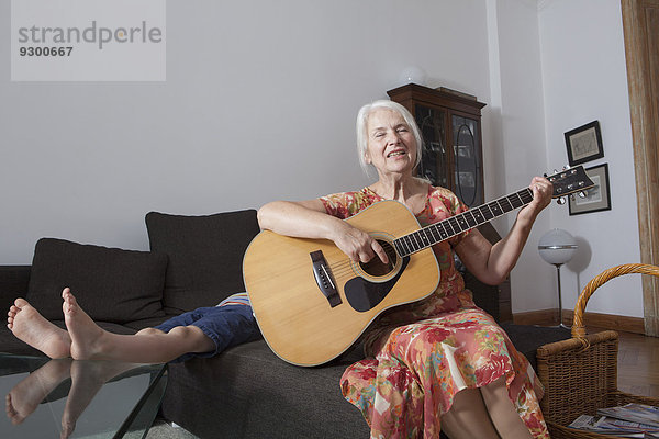 Seniorin singt Lied  während sie zu Hause Gitarre spielt.
