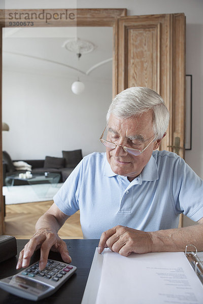 Älterer Mann  der die Hausfinanzen am Tisch berechnet.
