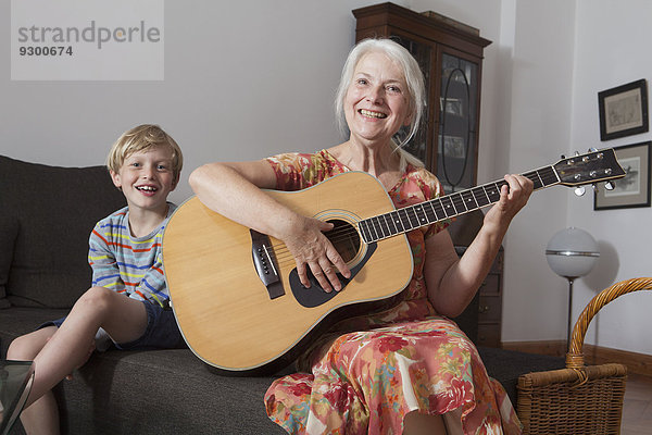 Porträt eines Jungen  der mit seiner Großmutter auf dem Sofa sitzt und Gitarre spielt.