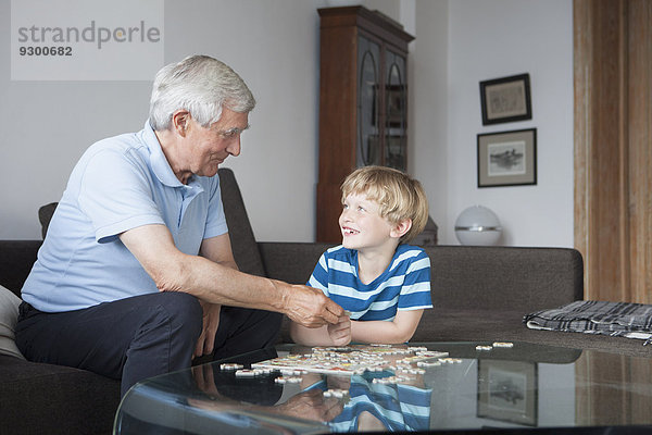 Glücklicher Enkel und Großvater schauen sich an und lösen Puzzle im Wohnzimmer.