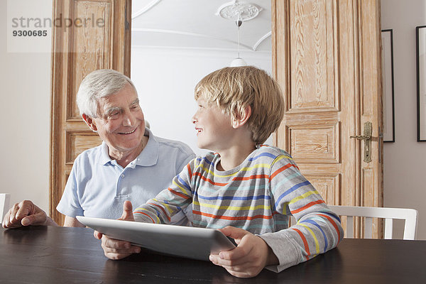 Glücklicher älterer Mann sieht Enkel mit digitalem Tablett zu Hause an