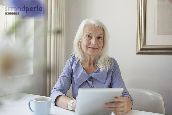 Porträt der selbstbewussten Seniorin mit digitalem Tablett am Tablett