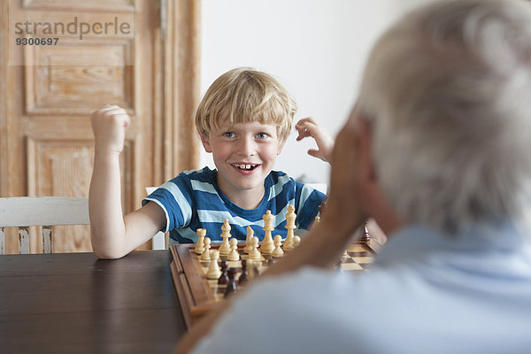 Glücklicher Enkel beim Schachspiel mit Großvater zu Hause