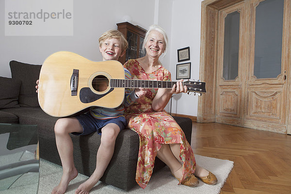 Glücklicher Enkel und Großmutter mit Gitarre zu Hause auf dem Sofa sitzend