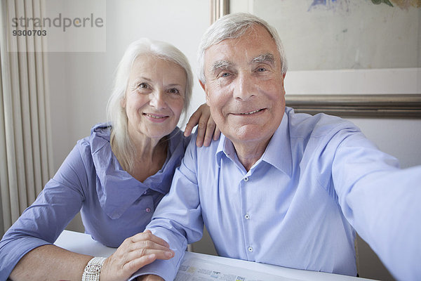 Porträt eines lächelnden Seniorenpaares  das zusammen am Tisch sitzt.