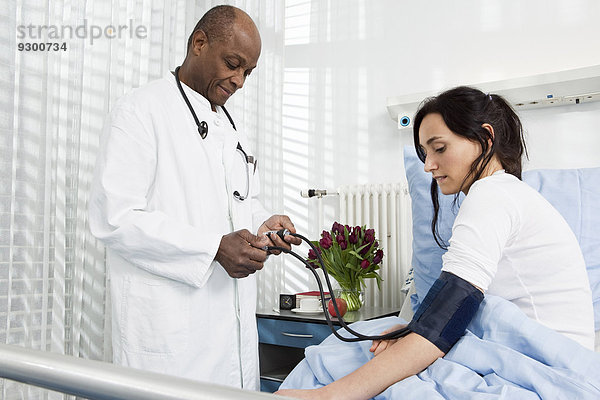 Ein Arzt  der den Blutdruck eines Patienten in einem Krankenhaus nimmt.