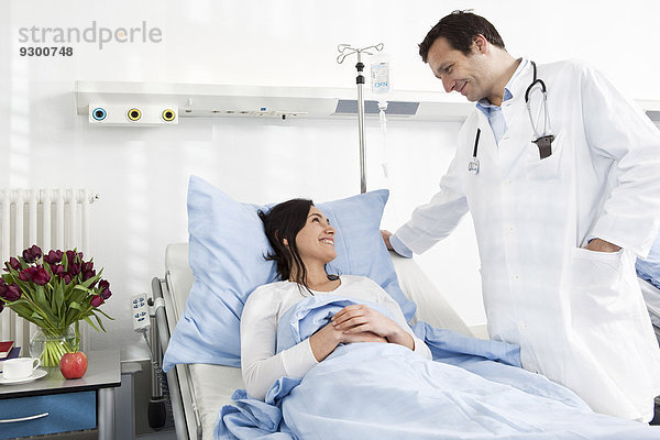 Ein Arzt im Gespräch mit einem lächelnden Patienten  der in einem Krankenhausbett liegt.
