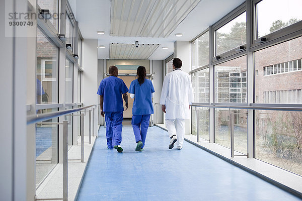 Drei Mediziner gehen gemeinsam einen Gang in einem Krankenhaus entlang  Rückansicht