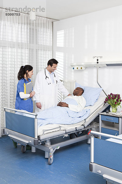 Ein Arzt und eine Krankenschwester im Gespräch mit einem Patienten  der in einem Krankenhausbett liegt.