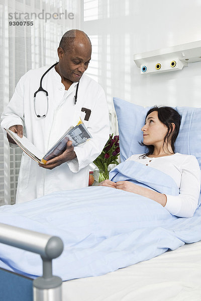 Ein Arzt im Gespräch mit einem Patienten  der in einem Krankenhausbett liegt.