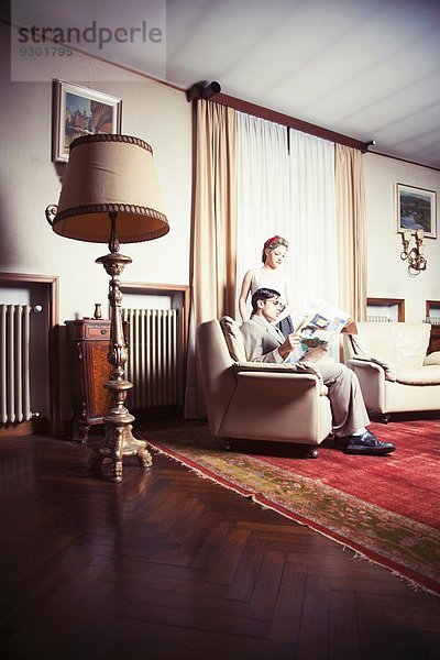 Porträt eines jungen Vintage-Paares im Wohnzimmer beim Zeitungslesen