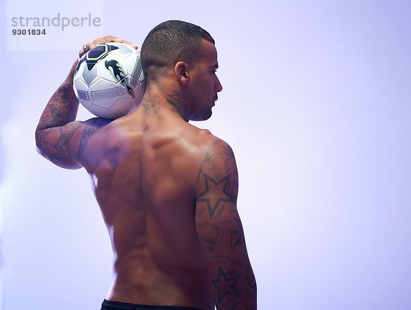 Studioaufnahme eines jungen männlichen Fußballspielers  der den Ball auf der Schulter hält.
