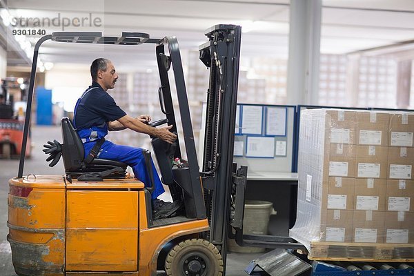 Erwachsener Mann mit Gabelstapler in der Fabrik