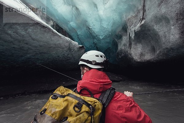 Mann überquert Fluss mit Seil in Eishöhle  Vatnajokull Gletscher  Vatnajokull Nationalpark  Island