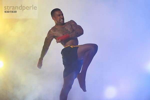 Studioaufnahme eines muskulösen männlichen Kickboxers im Scheinwerferlicht und Nebel