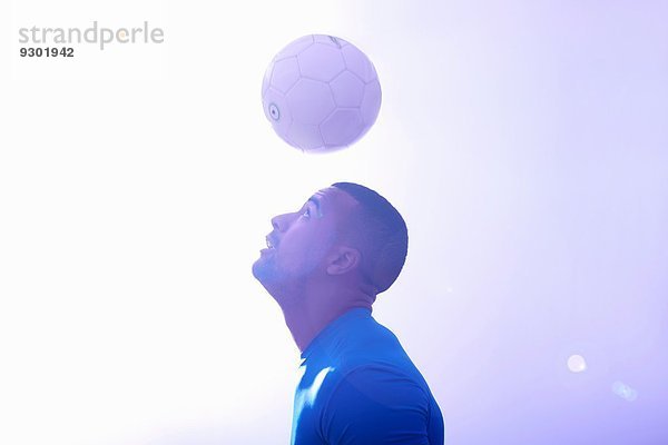 Studioaufnahme eines jungen männlichen Fußballspielers  der den Ball in der Luft hält  mit Kopfball