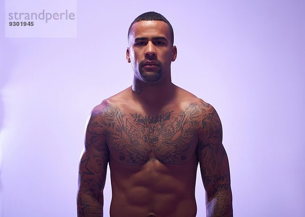 Studio-Porträt eines muskulösen Sportlers mit nackter Brust und Tattoos
