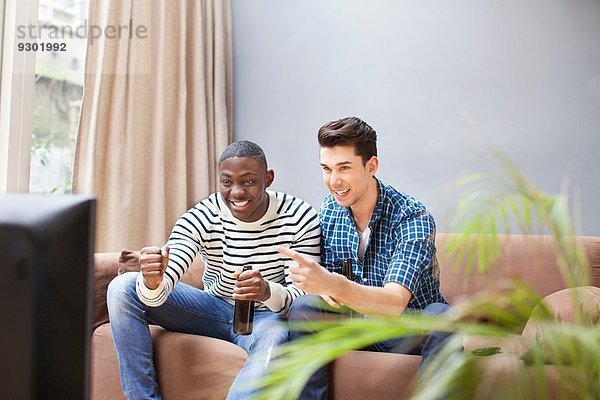 Zwei junge Männer  die Bier trinken und im Wohnzimmer fernsehen.