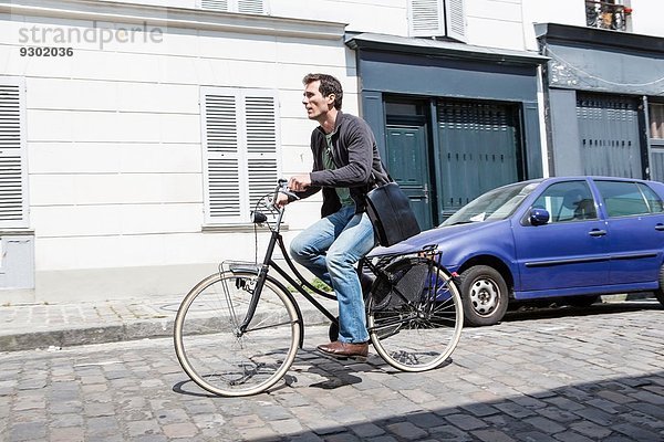 Mittlerer Erwachsener Mann  der mit dem Fahrrad die gepflasterte Stadtstraße hinunterfährt.