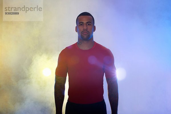 Studio-Porträt eines muskulösen jungen Sportlers im Scheinwerferlicht und Nebel