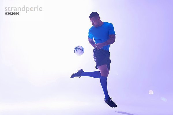 Studioaufnahme eines jungen männlichen Fußballspielers  der mit Rückstoß den Ball in der Luft hält.