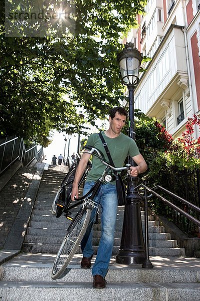 Mittlerer Erwachsener  der ein Fahrrad die Treppe hinunter trägt  in Paris  Frankreich