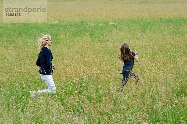 Mutter und Tochter rennen durch langes Grasfeld