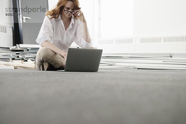 Mittlere erwachsene Geschäftsfrau mit Laptop auf dem Boden in neuem Büro