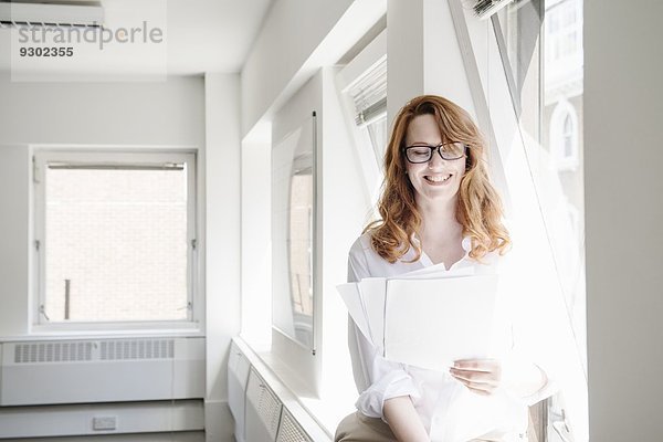 Mittlere erwachsene Geschäftsfrau beim Lesen von Papierkram im Büro