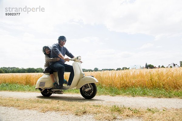 Erwachsener Mann und Tochter fahren Motorroller entlang der Schotterpiste