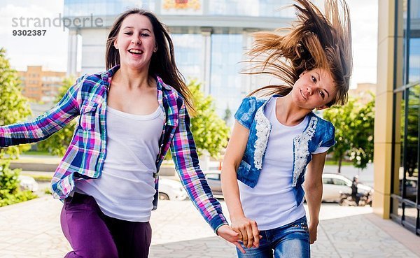 Zwei junge Frauen  die ihre Haare schütteln und in der Stadt rennen.